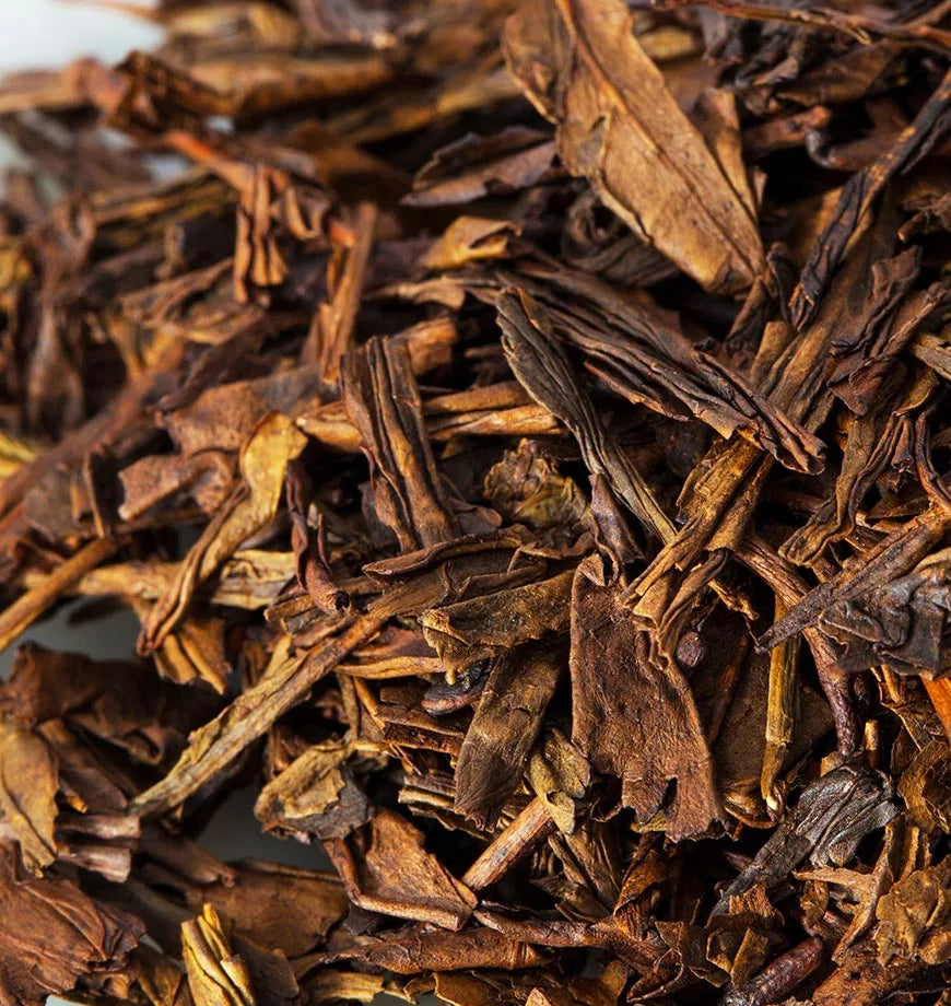 A pile of dried leaves from Houjicha, an organic green tea, arranged on a white surface.