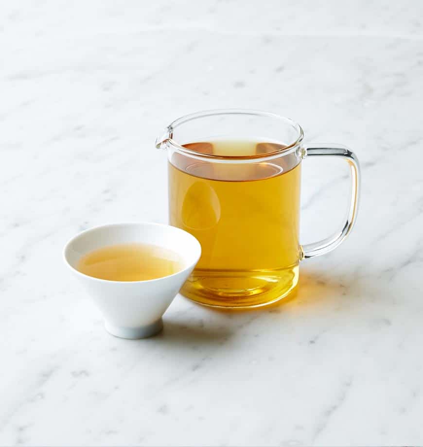 A cup filled with cacao mint tea and a pitcher of tea on a sleek marble countertop.