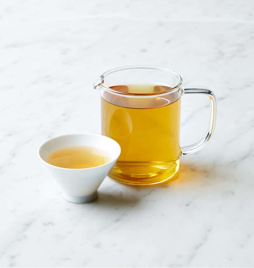 A cup and pitcher of Spearmint Sage tea resting on a smooth marble surface.