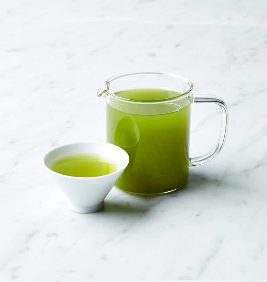 A pitcher and cup of organic green tea, Ryokucha, displaying the refreshing green color of the brewed beverage.