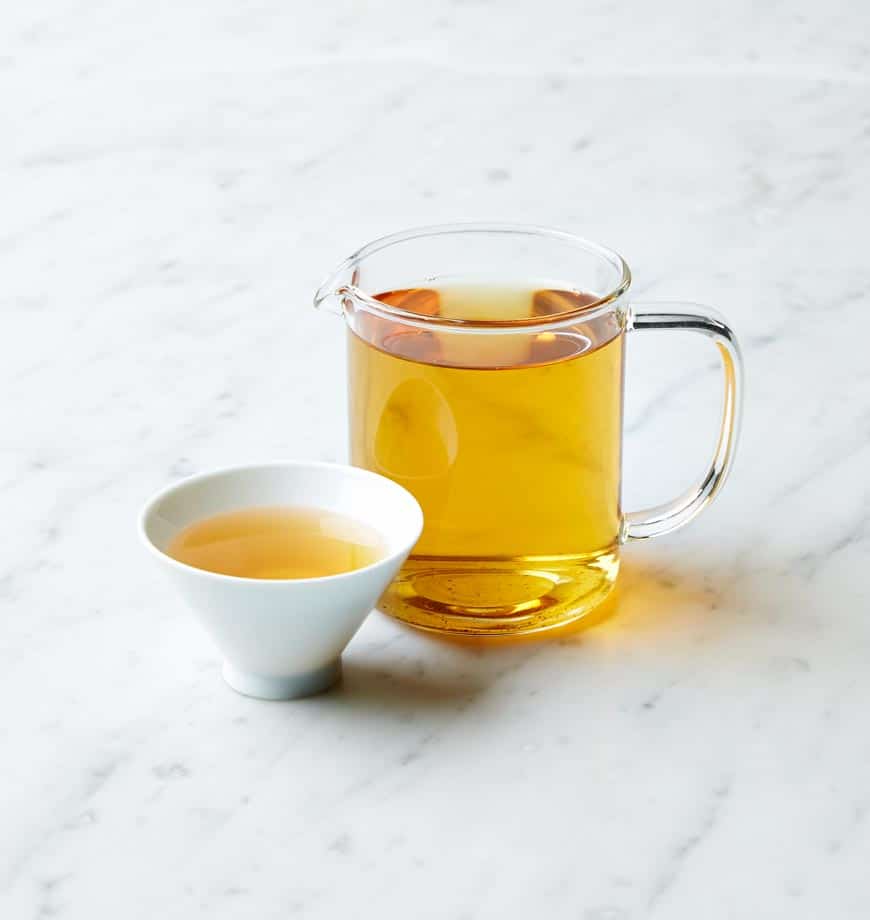 A cup and pitcher of oolong tea displayed on a marble surface