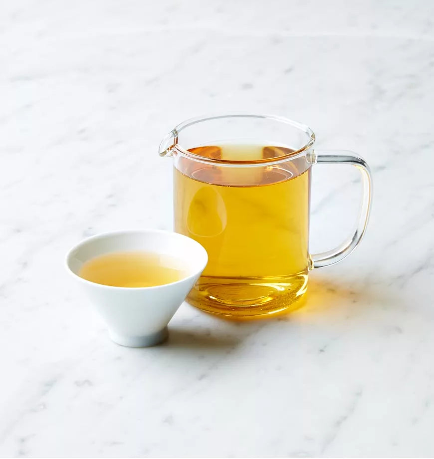 A cup of Persian tea and a pitcher of tea sit on a marble counter, showcasing a warm and inviting beverage setting.