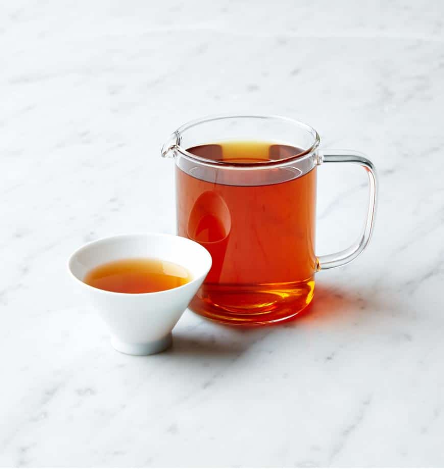 A cup of Bodacious Black Tea and a pitcher of tea on a polished marble counter.
