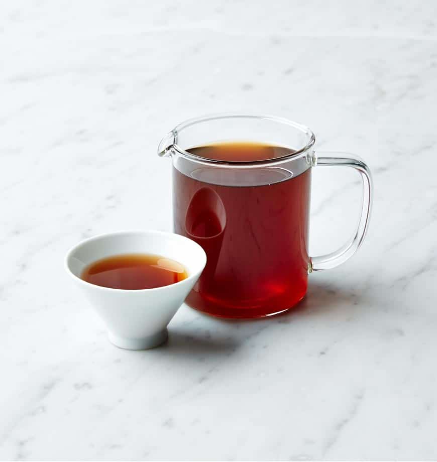 A cup and pitcher of Blood Orange organic pu erh tea on a polished marble counter.
