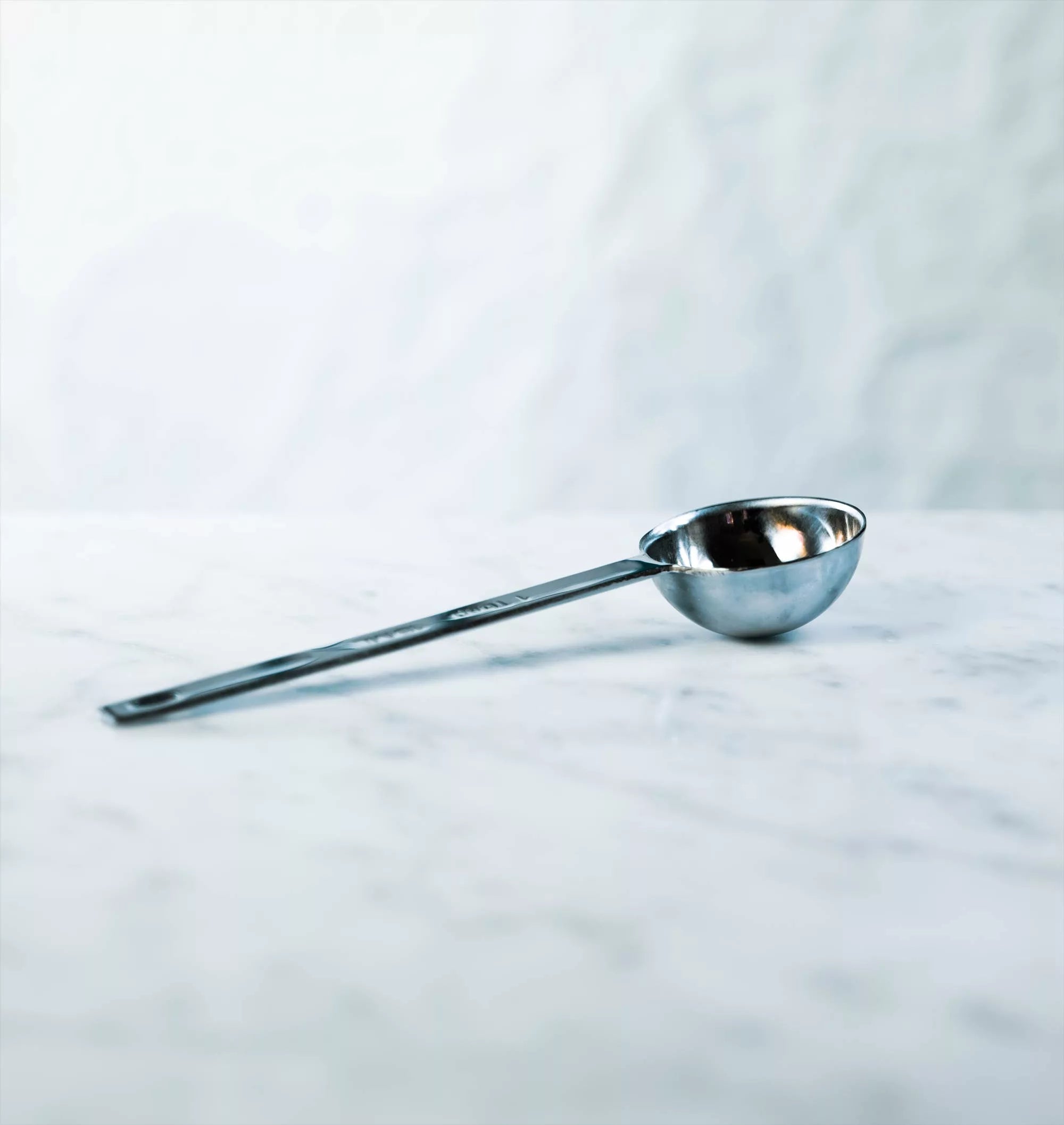 A shiny stainless steel measuring spoon atop a marble counter.