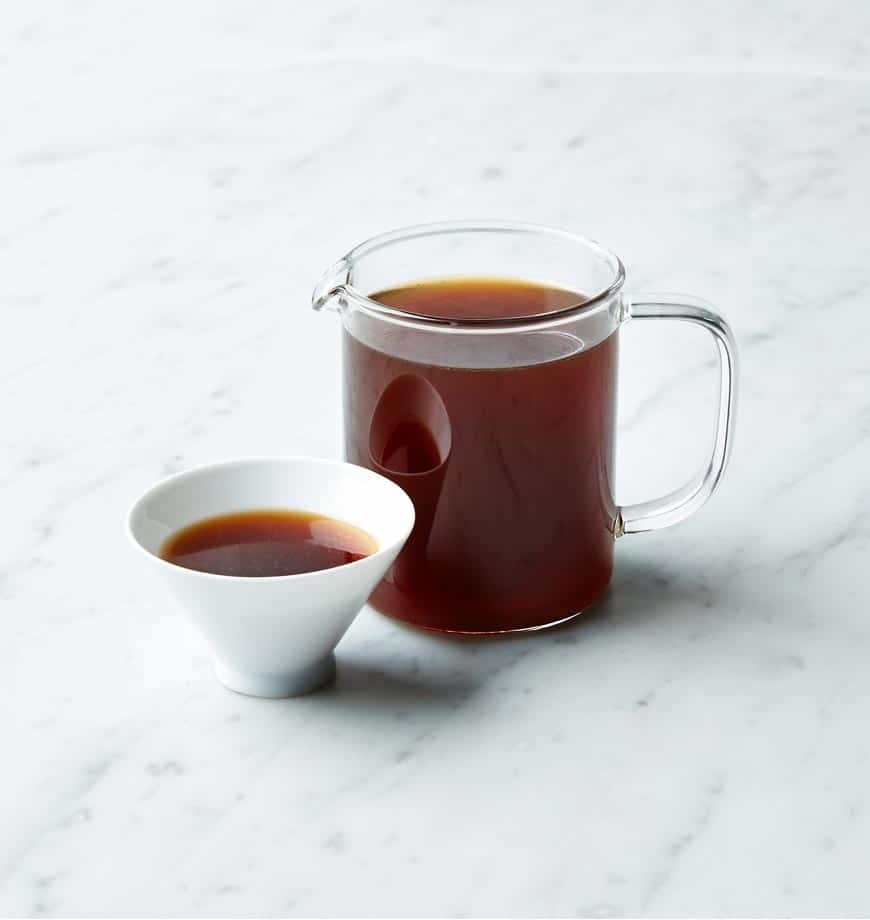 A pitcher of Velvet Cacao organic pu erh tea beside a steaming cup of tea on a wooden table.