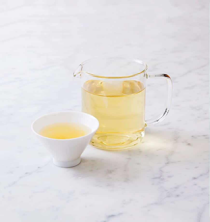 A pitcher of green tea and a cup of chamomile blossom herbal tea arranged on a wooden tabletop